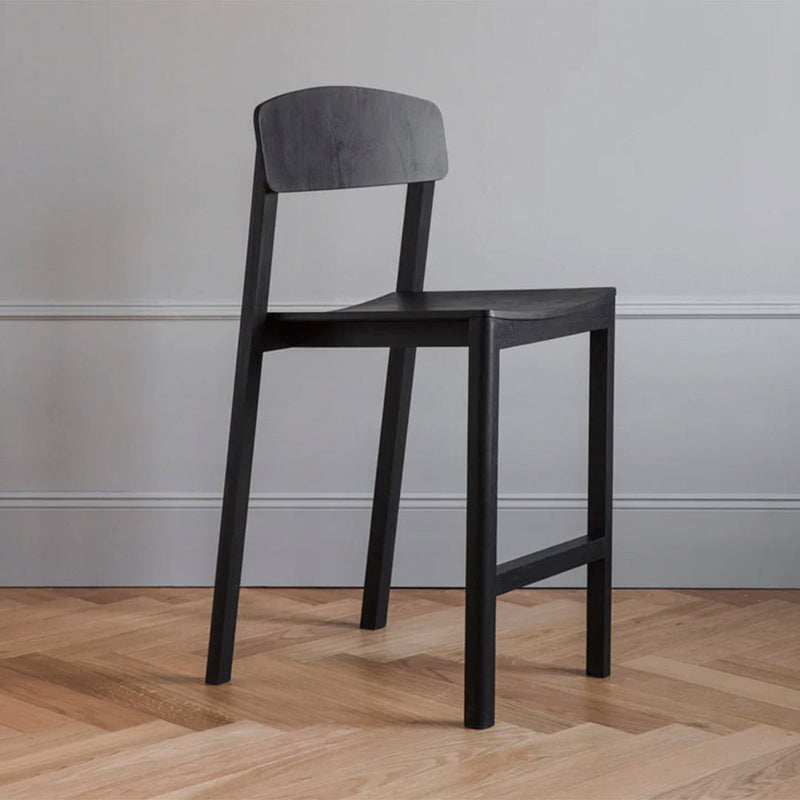Black wooden chair with a minimalist design and smooth finish against a light grey wall and herringbone wood floor.