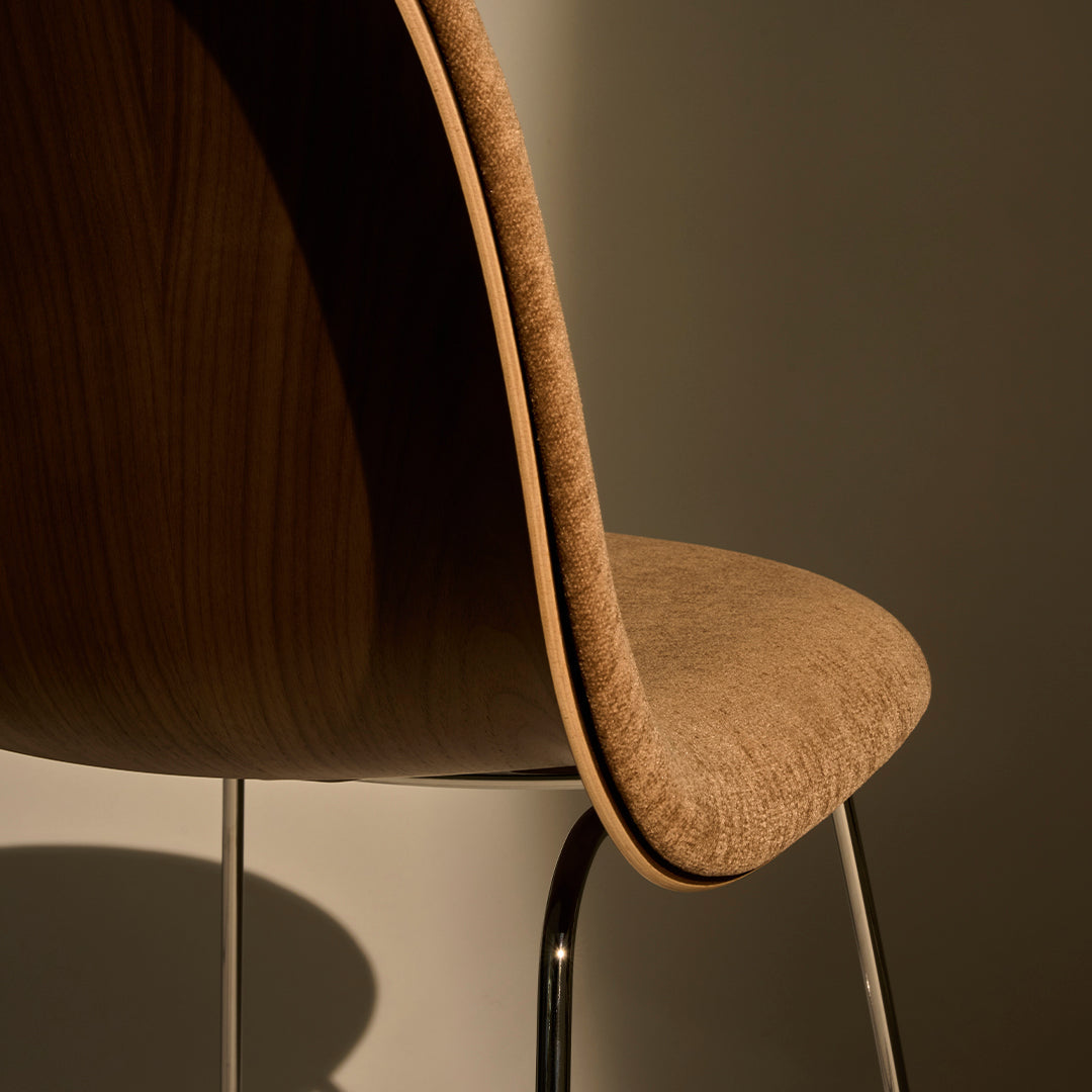 Brown textured chair with a curved wooden backrest and sleek silver legs against a soft neutral background.