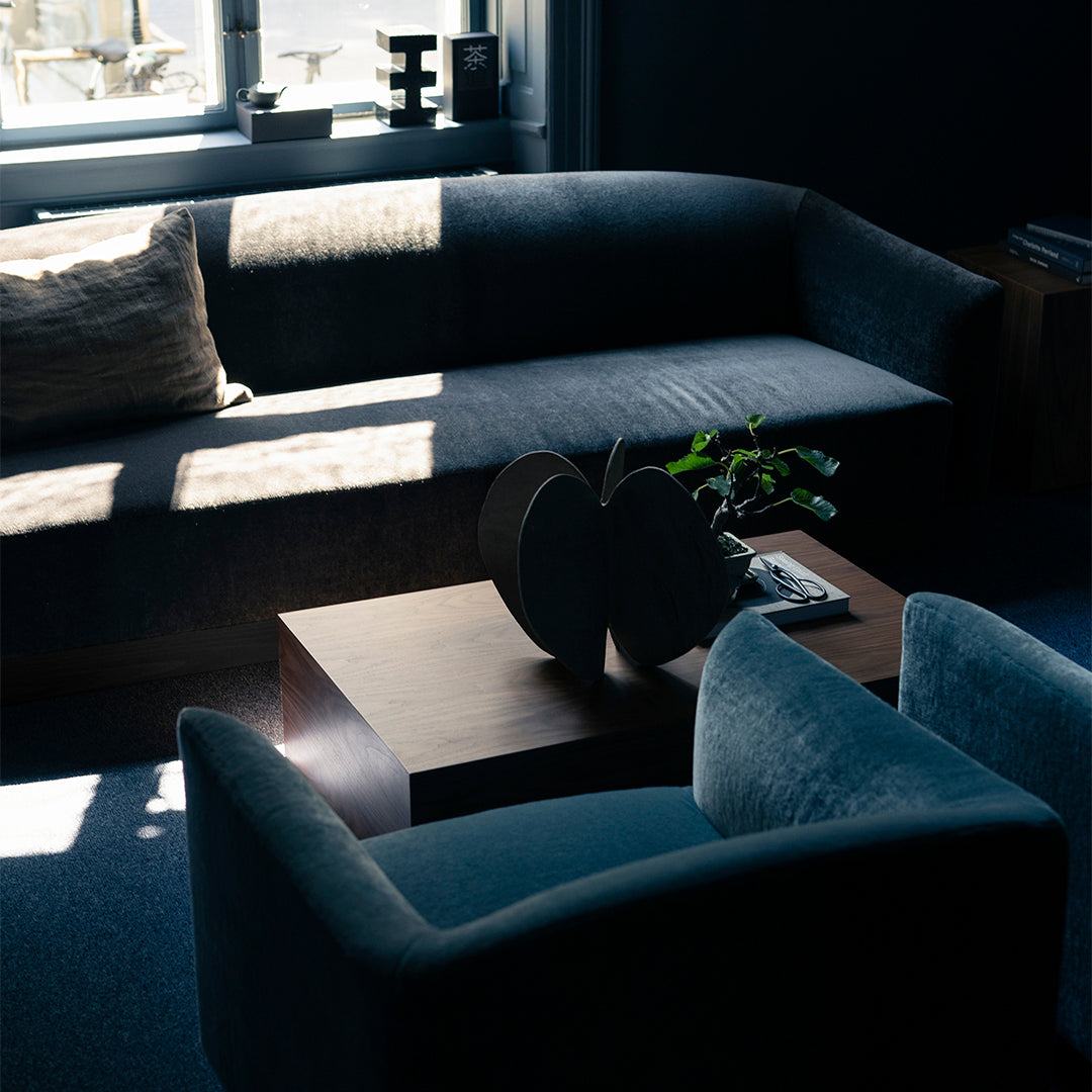 Stylish dark gray sofa with light cushions and soft teal accent chairs in a modern living space.