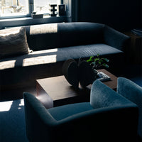 Stylish dark gray sofa with light cushions and soft teal accent chairs in a modern living space.