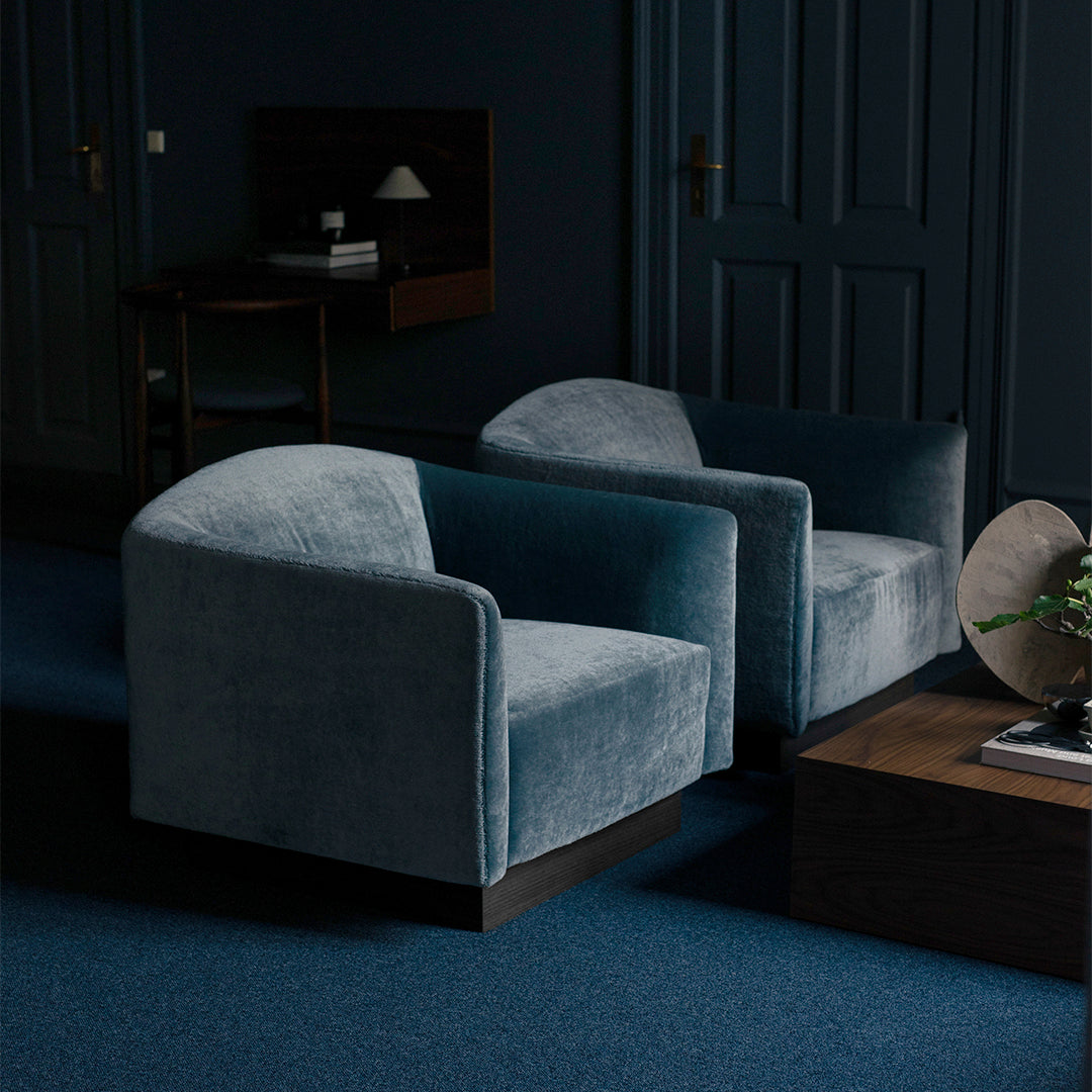 Velvet chairs in soft teal with curved backs, set against dark blue walls and a matching carpet. Modern and stylish design.