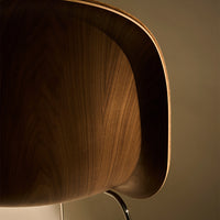 Close-up of a sleek wooden chair with rich walnut tones and subtle grain patterns, highlighted by soft ambient lighting.