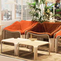 "Orange fabric chairs with soft curves, paired with minimalist white tables on a beige carpet."