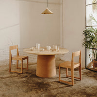Natural wood dining table with a circular top, paired with simple wooden chairs in a soft, neutral color palette.