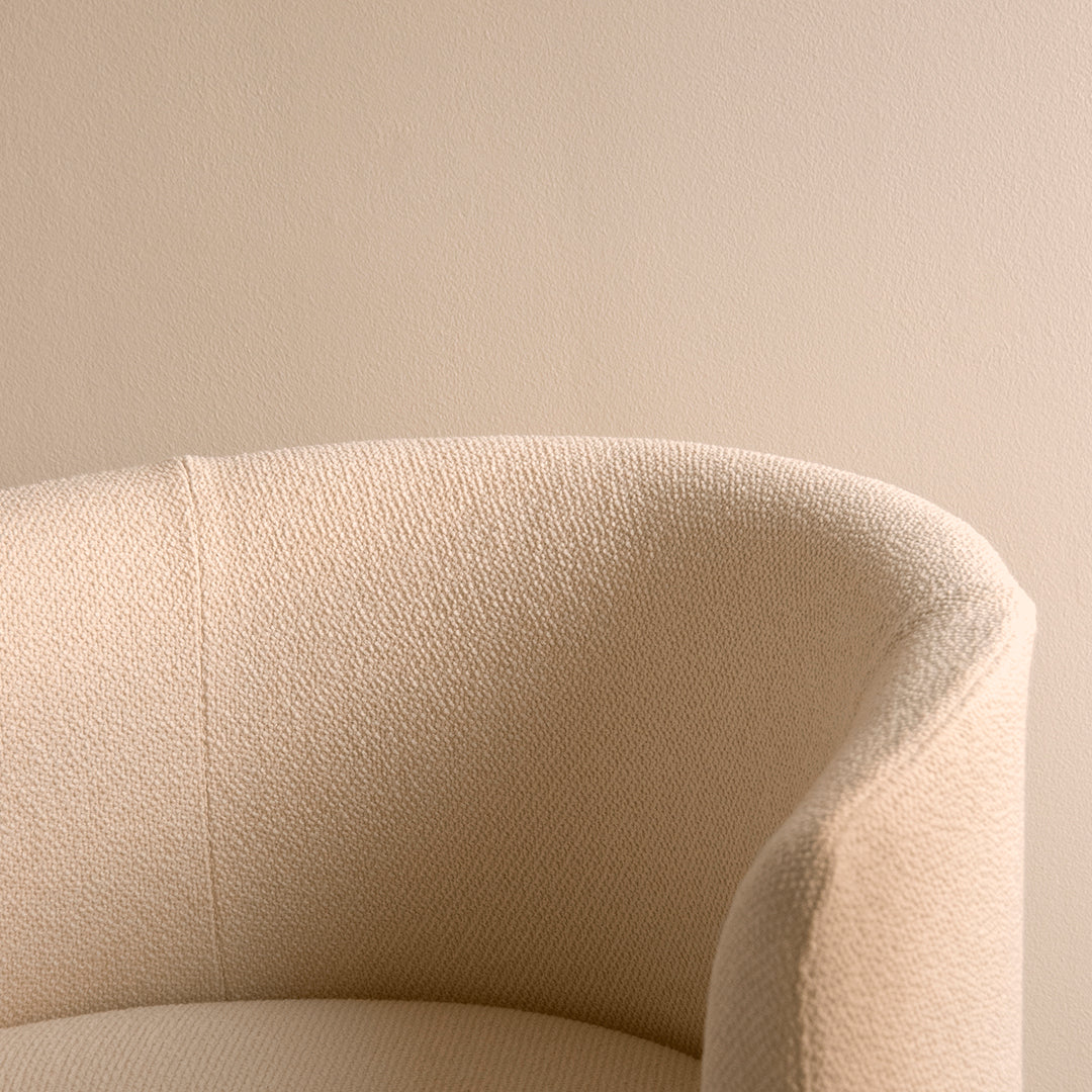Beige textured upholstery on a curved armchair against a soft neutral wall background.