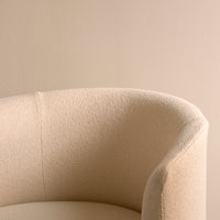 Beige textured upholstery on a curved armchair against a soft neutral wall background.