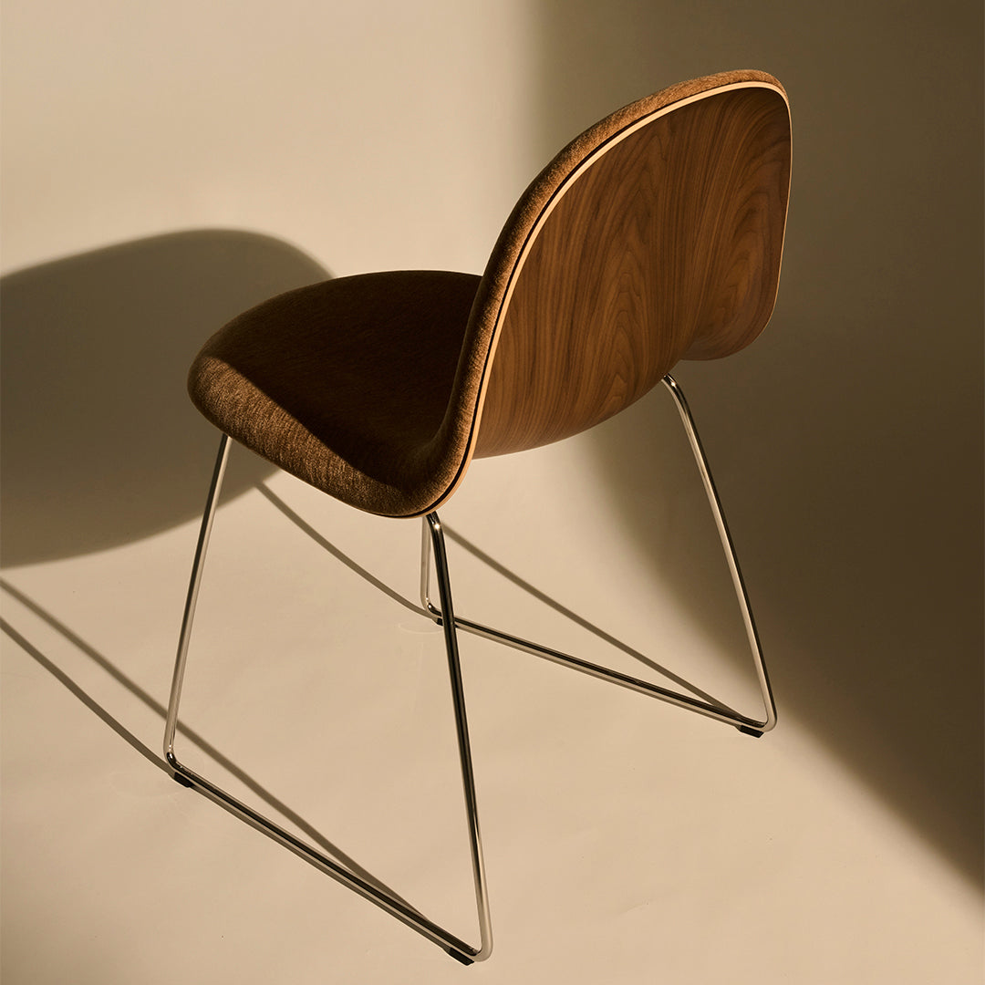 Brown wooden chair with a sleek, curved backrest and chrome legs, set against a soft beige background.