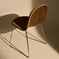 Brown wooden chair with a sleek, curved backrest and chrome legs, set against a soft beige background.