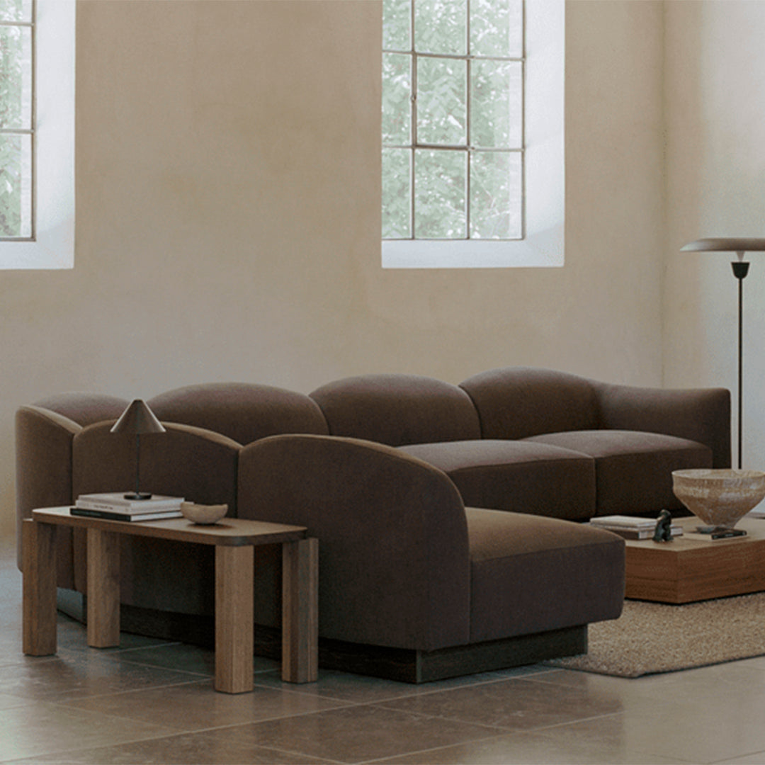 Modern brown sectional sofa with smooth curves and a chic design, complemented by a beige and wooden coffee table.