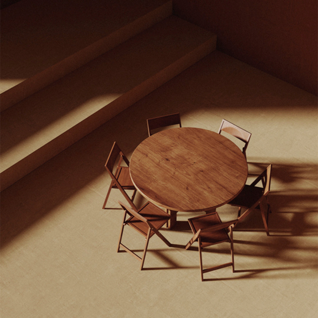 Wooden round table with minimalist design and light brown chairs against a warm, neutral-toned backdrop.