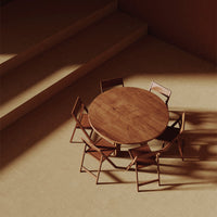 Wooden round table with minimalist design and light brown chairs against a warm, neutral-toned backdrop.