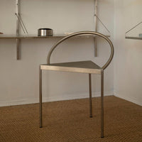 Sleek silver chair with a minimalist design and a geometric pattern, featuring a curved back and triangular seat.