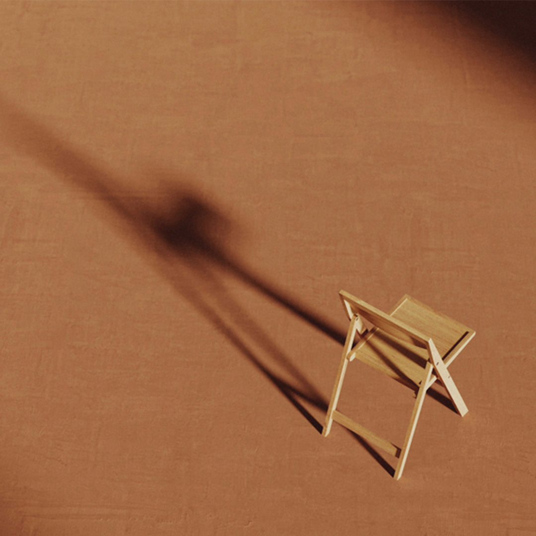 Light wooden folding chair on a warm, earthy brown backdrop with soft shadows creating depth.