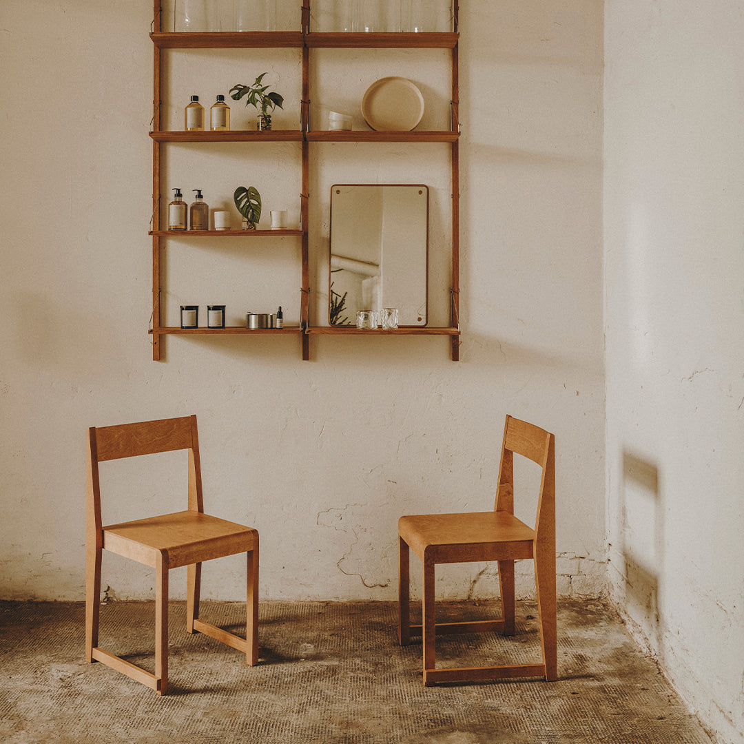 "Two simple wooden chairs in a natural wood finish against a light, textured wall, featuring minimalistic decor."