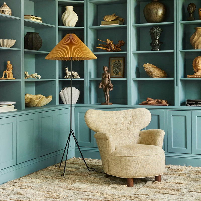 Beige armchair with a textured pattern against a teal backdrop and a warm yellow pleated lampshade. Stylish home decor.