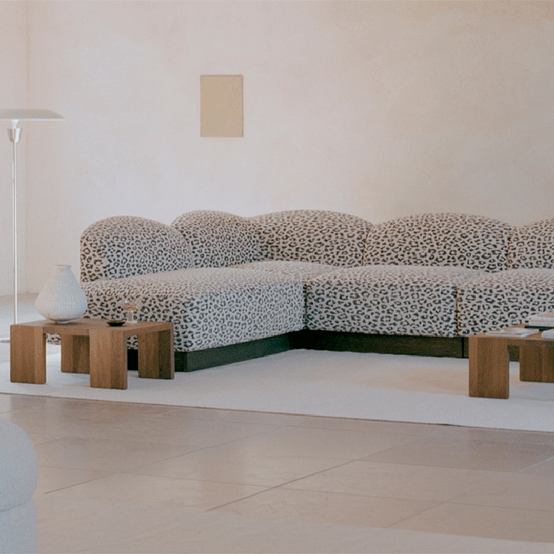 Black and white spotted fabric sectional sofa with green base in a minimalist room setting.
