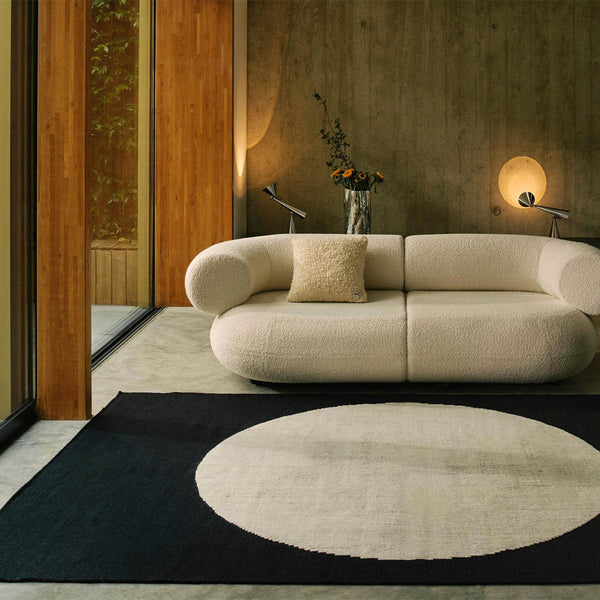 Textured cream couch on a black rug featuring a large white circular pattern, set against a modern interior backdrop.