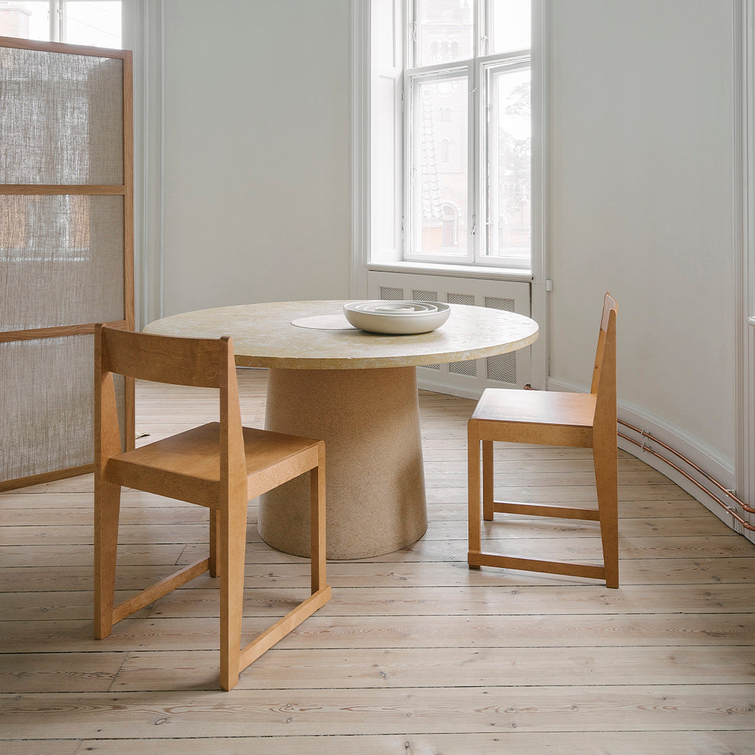 Stylish round table with a natural wood finish, paired with simple wooden chairs in neutral tones, featuring a minimalist aesthetic.