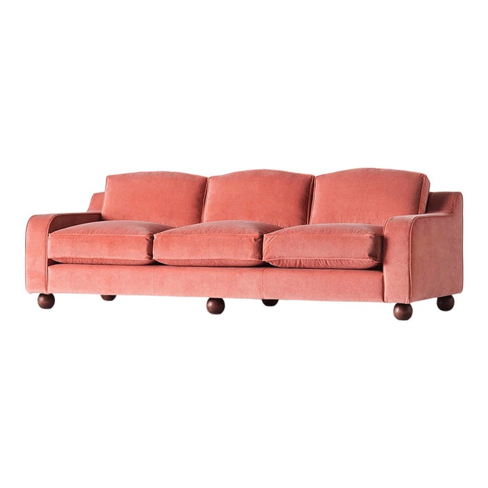 Blush pink velvet sofa with rounded cushions and dark wooden legs, featuring a smooth, minimalist design.