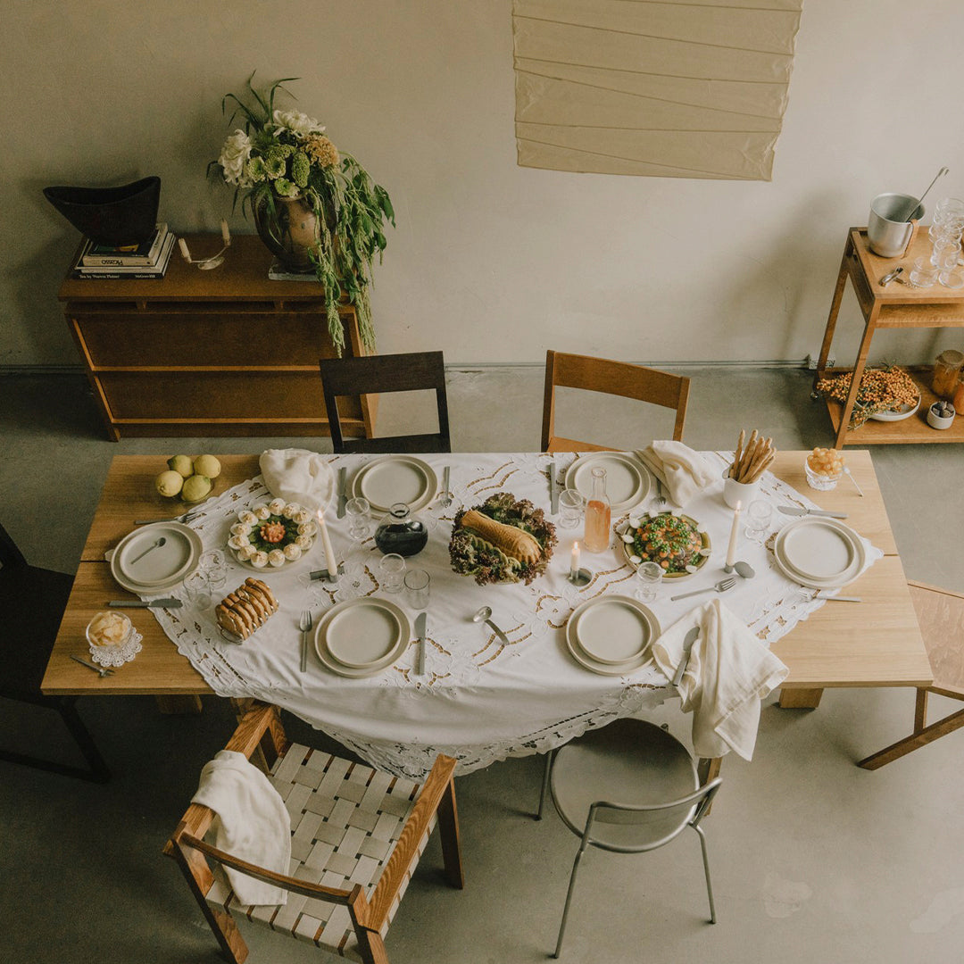 Elegant white tablecloth with a textured pattern, set against a backdrop of warm wood tones and soft greenery.