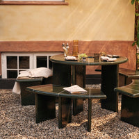 Green circular table with matching benches, featuring a smooth finish and minimalist design set in a gravel outdoor space.