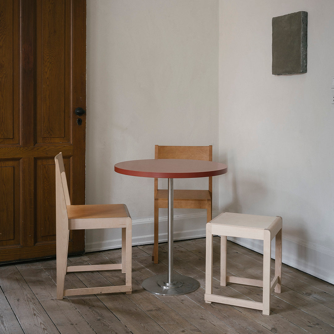 Modern minimalistic dining set with a round red table and natural wood chairs, featuring simple lines and neutral tones.