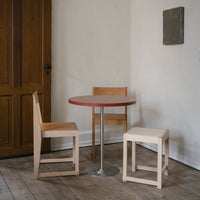 Modern minimalistic dining set with a round red table and natural wood chairs, featuring simple lines and neutral tones.