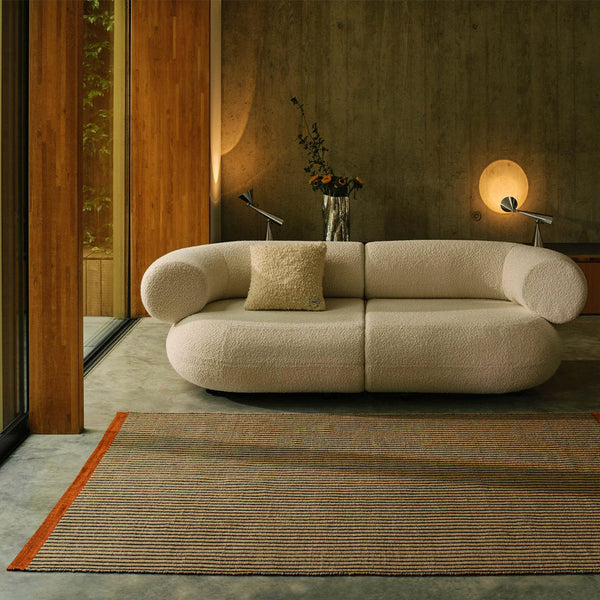 Cream-colored sofa with a textured finish, accompanied by a tan and orange striped rug in a modern setting.