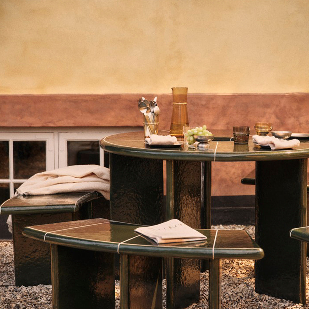"Dark green glossy table set with light beige fabrics and subtle geometric patterns, perfect for outdoor gatherings."