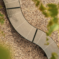 Curved stone path with gray tiles against a textured gravel backdrop, accented by green foliage.