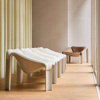 Minimalist chairs in white and cream hues, with a contrasting brown accent chair, set against soft yellow curtains.