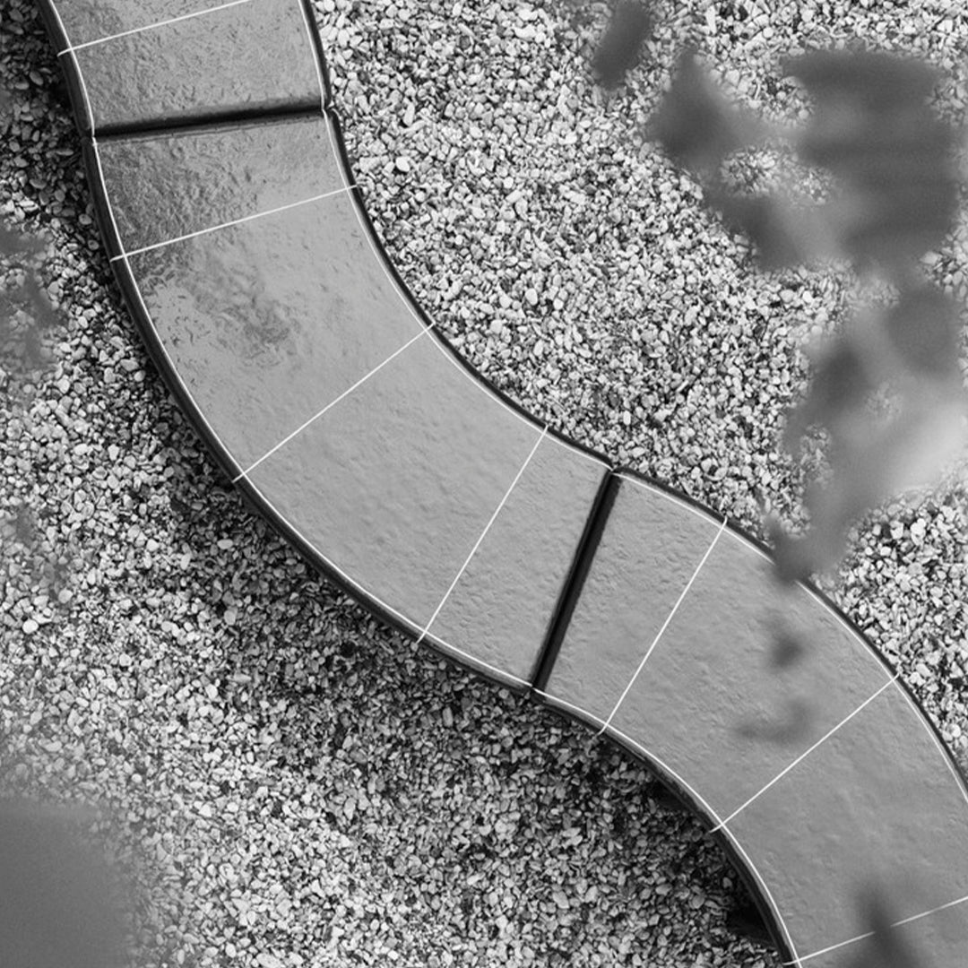 "Curved gray stone pathway over contrasting light gravel, featuring distinct panel patterns in black and white."