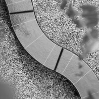 "Curved gray stone pathway over contrasting light gravel, featuring distinct panel patterns in black and white."