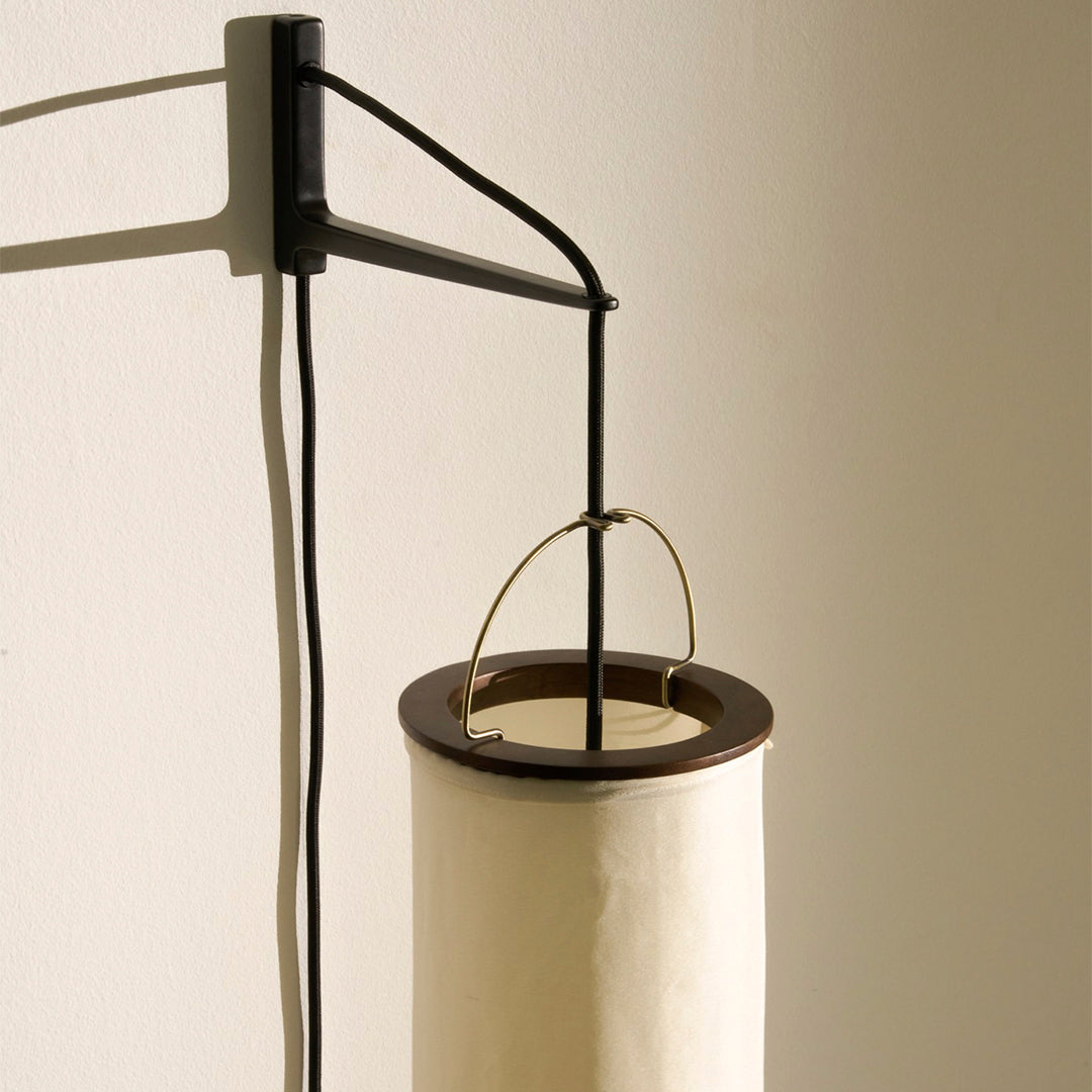 "Minimalist lamp with a black metal frame and a cream-colored cylindrical shade, featuring a smooth finish."