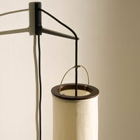 "Minimalist lamp with a black metal frame and a cream-colored cylindrical shade, featuring a smooth finish."