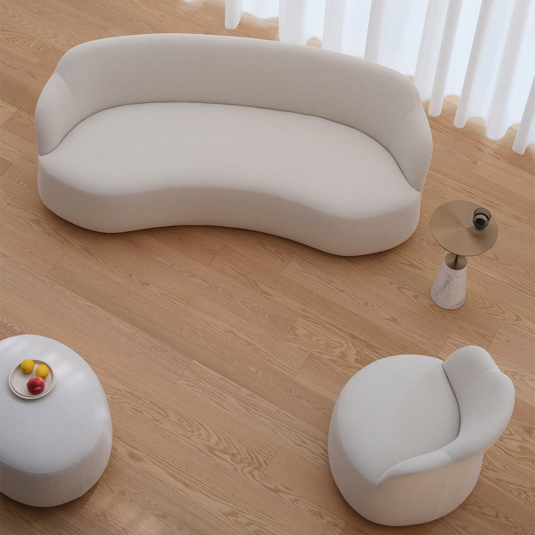 Curved cream sofa and cozy armchair on light wooden floor, featuring soft textures with minimalistic design.