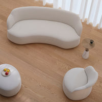 Curved cream sofa and cozy armchair on light wooden floor, featuring soft textures with minimalistic design.