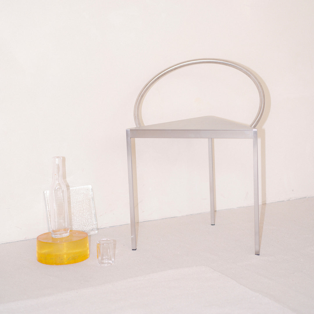 Silver transparent chair with a modern circular design, accompanied by clear and yellow glass vases on a neutral background.