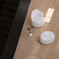 White modern chair and pouf on light wooden floor with a black wall and copper-accented side table.