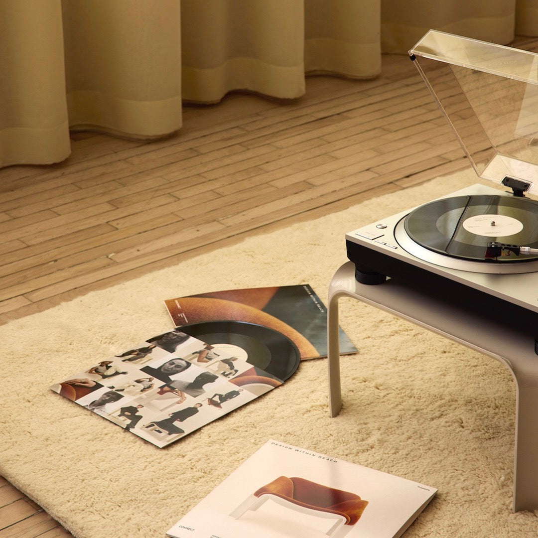 "Soft cream rug with wooden floor, featuring colorful vinyl record covers and a sleek black and silver turntable."