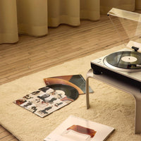 "Soft cream rug with wooden floor, featuring colorful vinyl record covers and a sleek black and silver turntable."