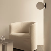Beige textured armchair against a soft, light wall, complemented by a sleek silver side table and glass.