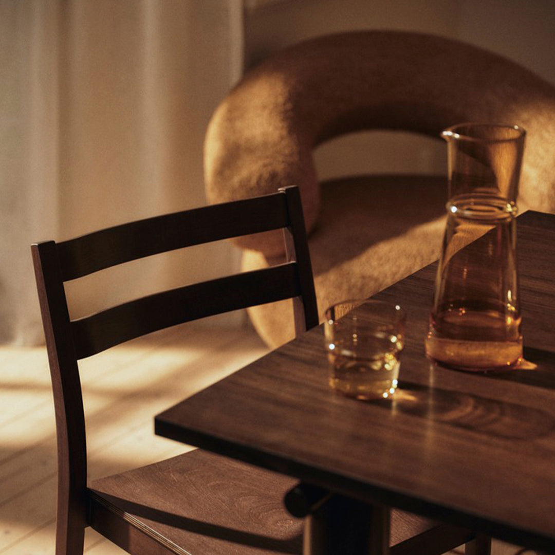 Wooden chair with rich brown tones, paired with a smooth, neutral-colored sofa and a glass pitcher.
