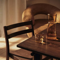 Wooden chair with rich brown tones, paired with a smooth, neutral-colored sofa and a glass pitcher.