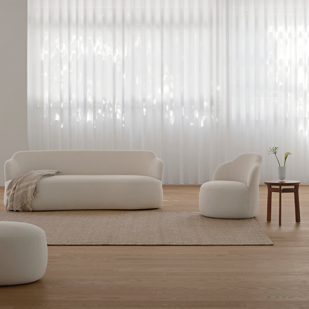 Cream upholstered sofa and chair on a beige area rug in a softly lit room with sheer white curtains.