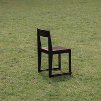 Black wooden chair with a simple design, featuring a smooth seat and straight lines, set against a grassy background.