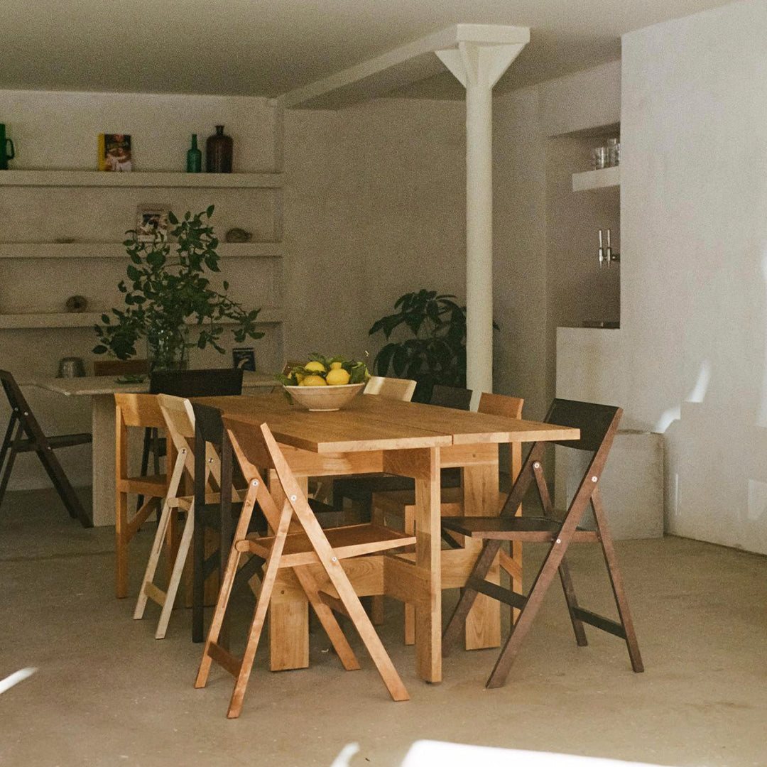 Light wood dining table with mixed-color folding chairs, featuring natural tones and minimalist design in a cozy interior.