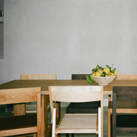 Wooden dining table with natural finishes and beige, brown, and gray chairs; minimalist style with a fresh lemon centerpiece.