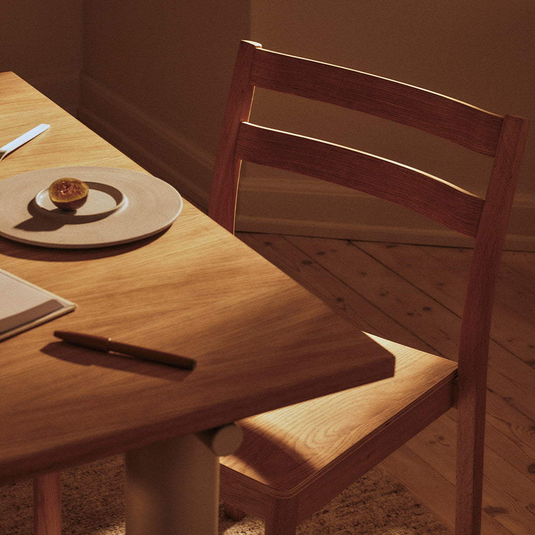 Warm wooden dining table with soft beige tones, featuring a simple round plate and a textured chair in natural wood grain.