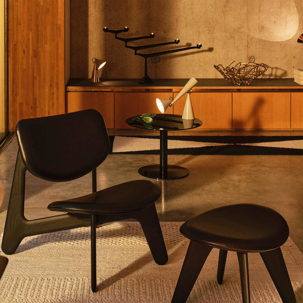 Elegant black-leather chair and stool on textured white rug, surrounded by warm wood and sleek black accents.